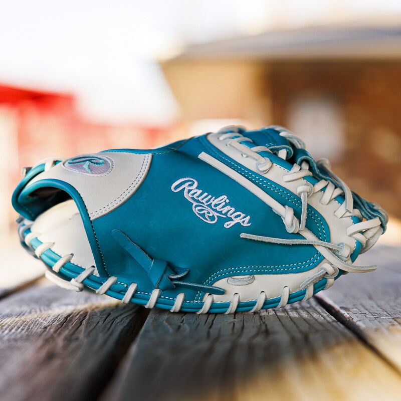 Picture of the thumb of a teal/white exclusive 33" Rawlings R2G Heart of the Hide catcher's mitt on a wood table