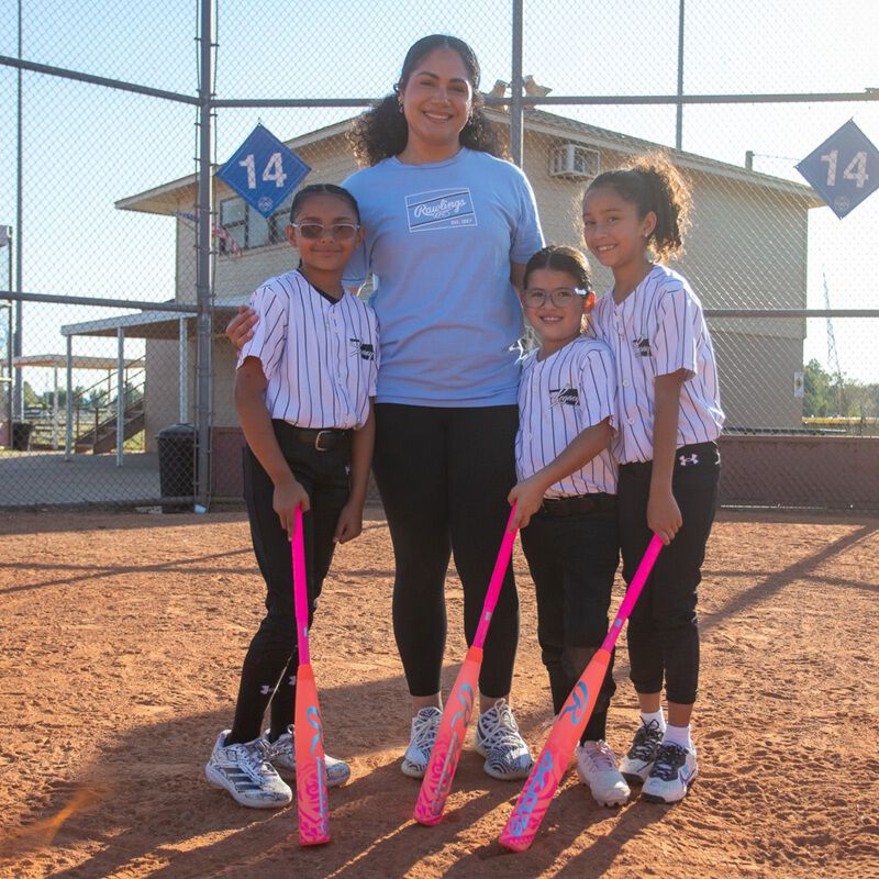 Jocelyn Alo and three young athletes standing together on a field with pink Rawlings ALO78 -12 fastpitch softball bats