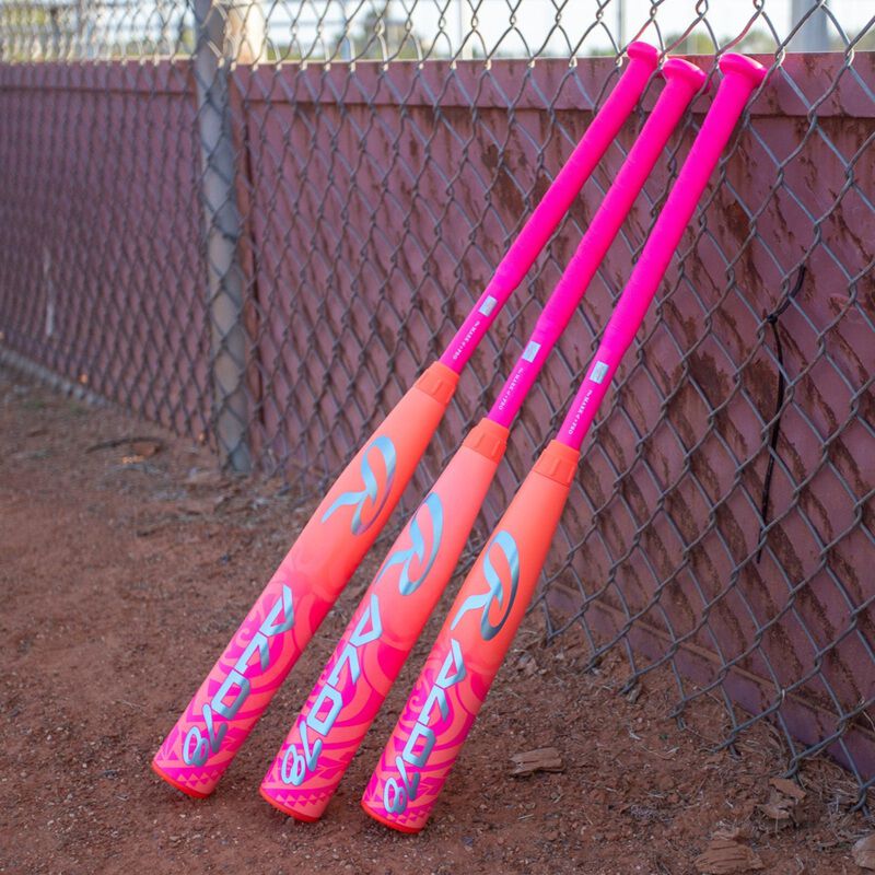 Three pink Rawlings ALO78 -12 fastpitch softball bats leaning against a fence