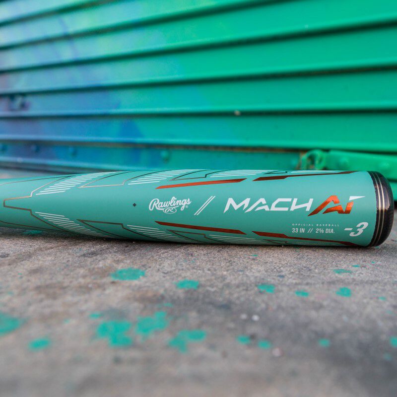 A Rawlings Mach AI BBCOR baseball bat laying on cement in front of a green wall - SKU: RBB4MC3