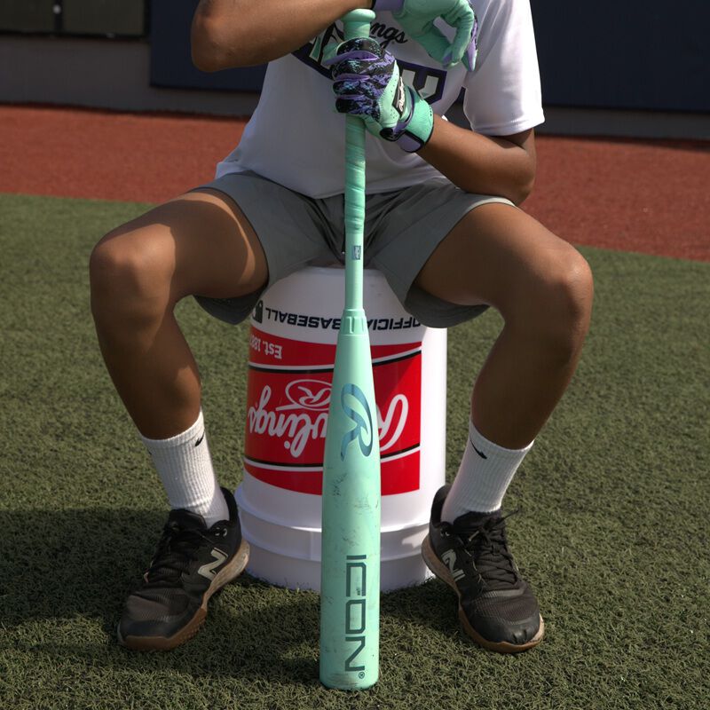 A player sitting on a bucket with a 2026 Rawlings Icon USSSA baseball bat loading=