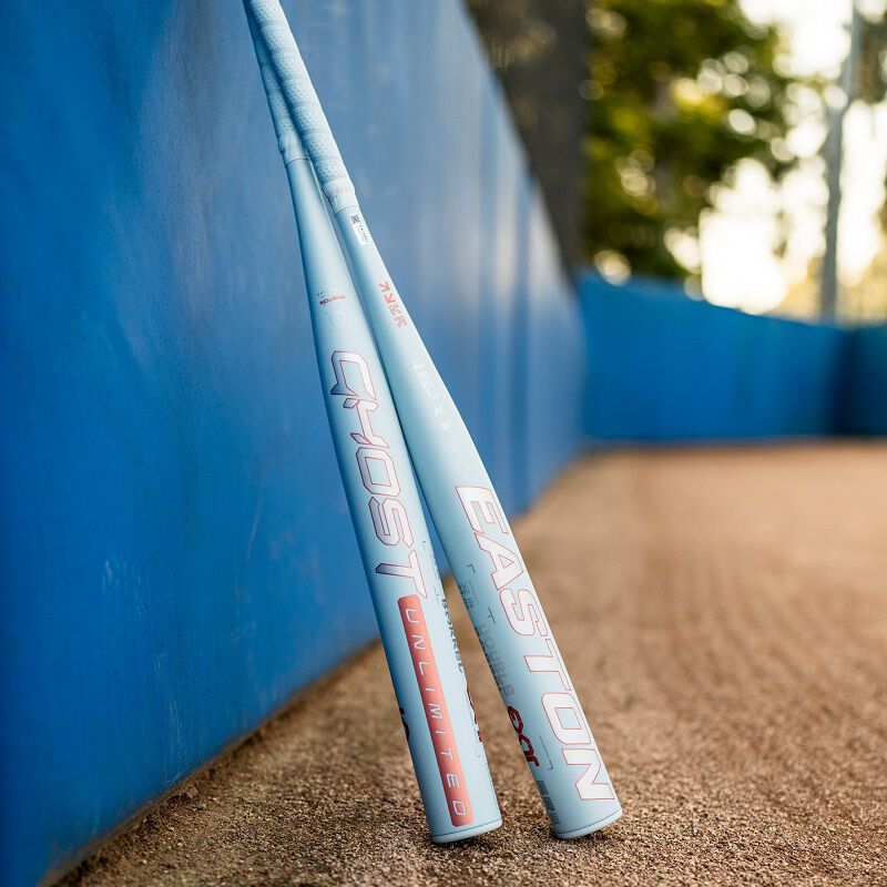A picture of 2 Easton Ghost Unlimited fastpitch bats standing up against a backstop