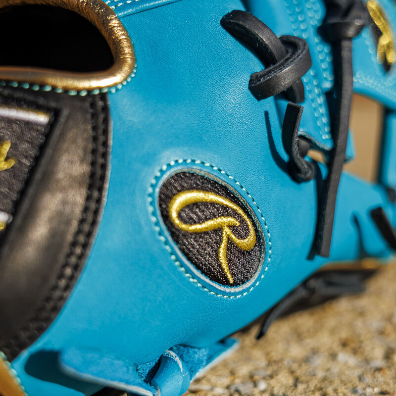 Picture of the black/gold Oval-R logo on the teal thumb of a Exclusive 11.5" Rawlings R2G Heart of the Hide infield glove