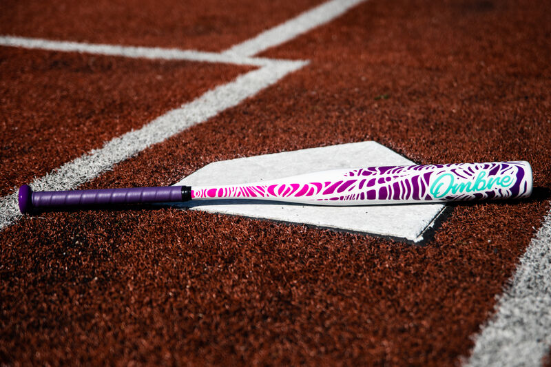 A Rawlings Ombre fastpitch bat lying on home plate of a field - SKU: FPZO11 loading=